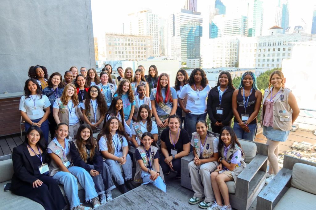 A large group of participants gathers on an outdoor terrace with city buildings in the background