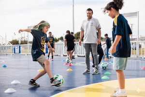 Landon Donovan watching a student practice soccer drills on a mini-pitch.