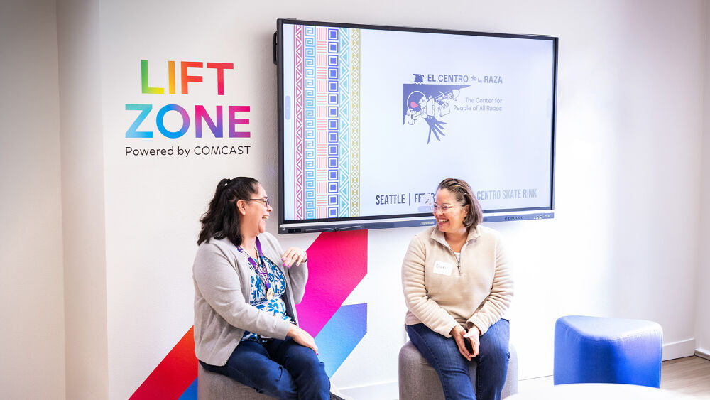 Two people sitting and talking in front of a mural that reads "Lift Zone