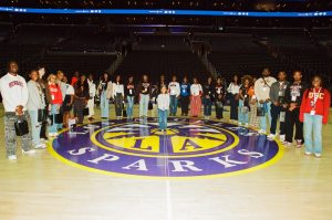 Group of students and professionals standing on the Los Angeles Sparks basketball court for a photo inside Crypto.com Arena.
