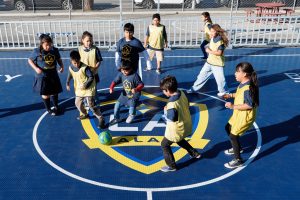 Children wearing LA Galaxy jerseys and pinnies play soccer around a ball on a branded mini-pitch court.