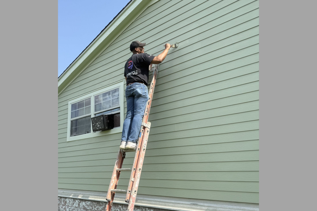 Volunteer on a ladder painting a house exterior
