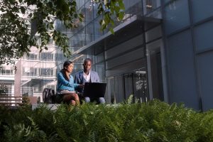 Two people sitting outside an office building looking at a laptop